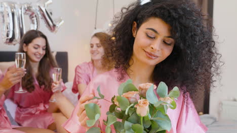 muslim woman holding bouquet, wearing pink silk nightdress, smiling and looking at camera