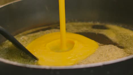scrambled eggs mixture being poured into pan with melted butter in slow motion with spatula. cooking breakfast ingredients food.