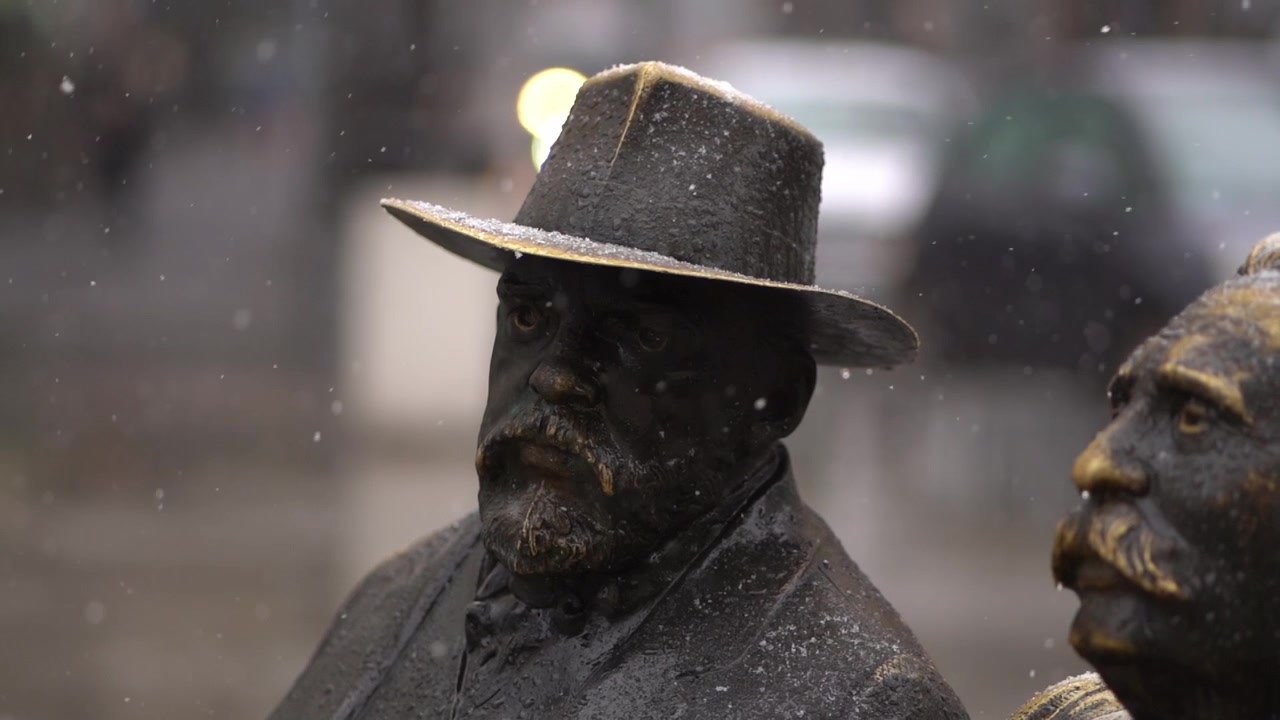 Snefald i slowmotion over slidte bronzestatuer af mænd siddende på en bænk