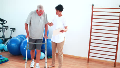 fisioterapeuta sonriente ayudando al paciente a caminar con el marco para caminar