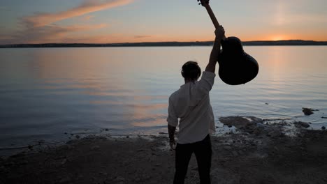 man with guitar at sunset by the lake