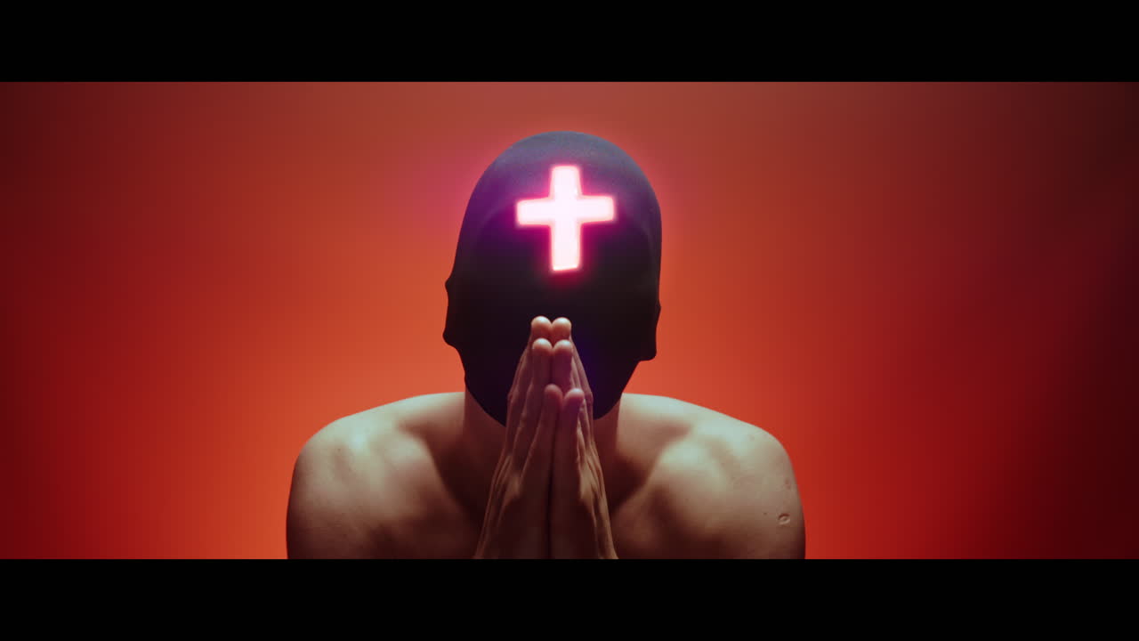 Masked man with cross of light glowing on his face nods gently