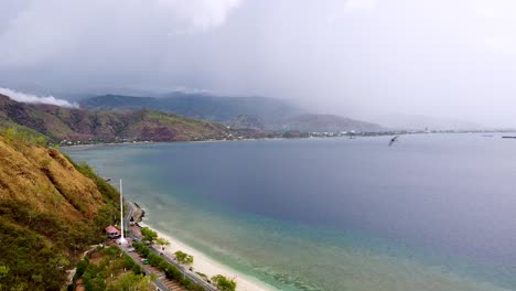 Aerial-drone-of-stunning-coastal-views,-hilly-landscape-and-blue-ocean-with-swallow-birds-flying-in-Dili,-Timor-Leste