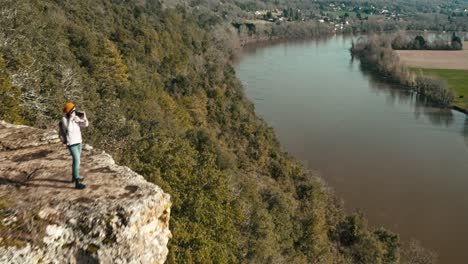 aerial view from away of a woman in nature taking photos at the edge of a cliff, the landscape is cultivated and wild