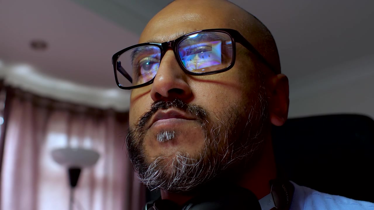 South asian male with beard wearing glasses working on computer with monitor reflecting in glasses