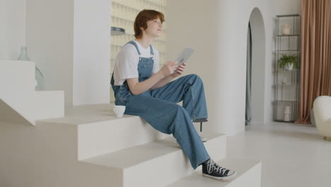 Side-View-Of-Girl-Sitting-On-The-Stairs-Watching-Something-On-A-Tablet-At-Home