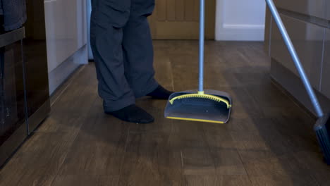 Male-Holding-Broom-And-Dustpan-Cleaning-Wooden-Floor-In-Kitchen