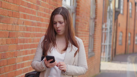 stressed and worried woman outdoors with financial worries about cost of living crisis debt and paying bills looking at mobile phone on city street 1