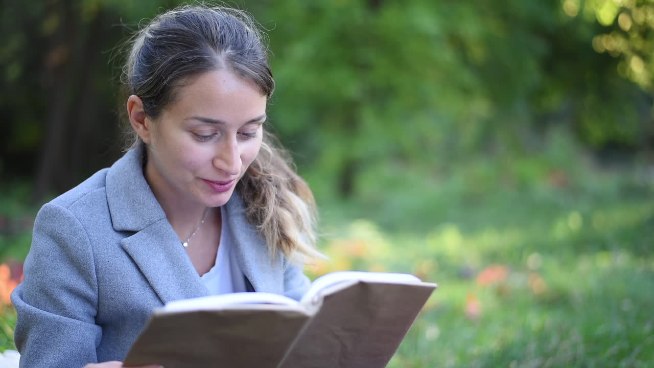 Blonde Frau liest ein Buch, während sie im Park auf dem Rasen liegt