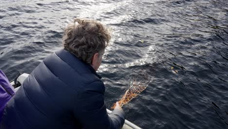 a man in his 40s hoists a crab net from the sea into a boat, handheld high angle