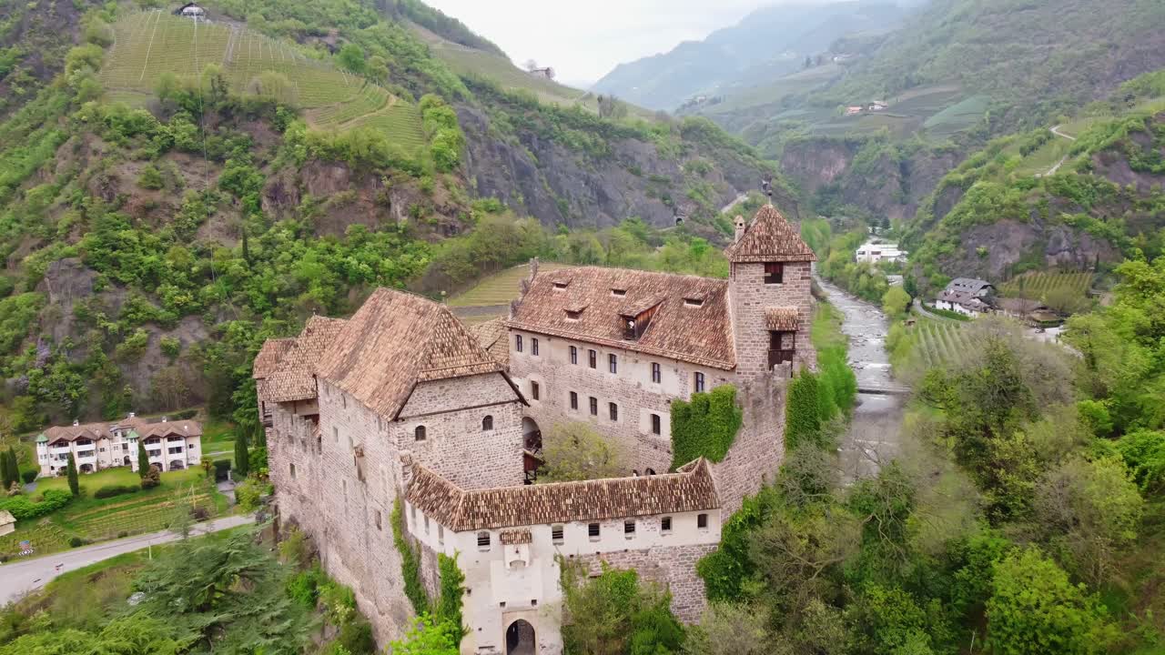 Smooth drone dolly shot flying forward toward Roncolo Castle, framed by greenery and mountains