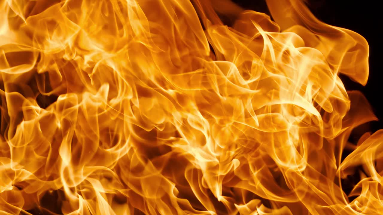 Levende nærbillede af hvirvlende orange flammende ild mod en mørk sort baggrund, der fanger dynamisk varme og bevægelse i abstrakt flammende tekstur. Optaget med super slowmotion-kamera med 1000 fps