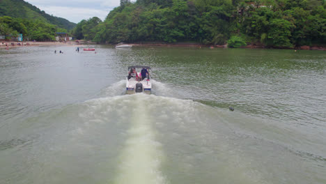 aerial tracking shot of small speedboat closing in the beach, vegetation in the background