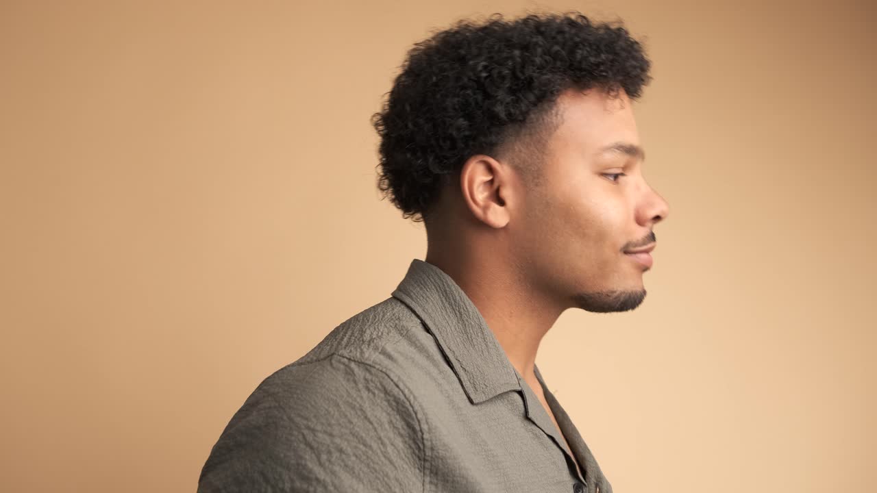 Happy young man smiling at camera in beige studio