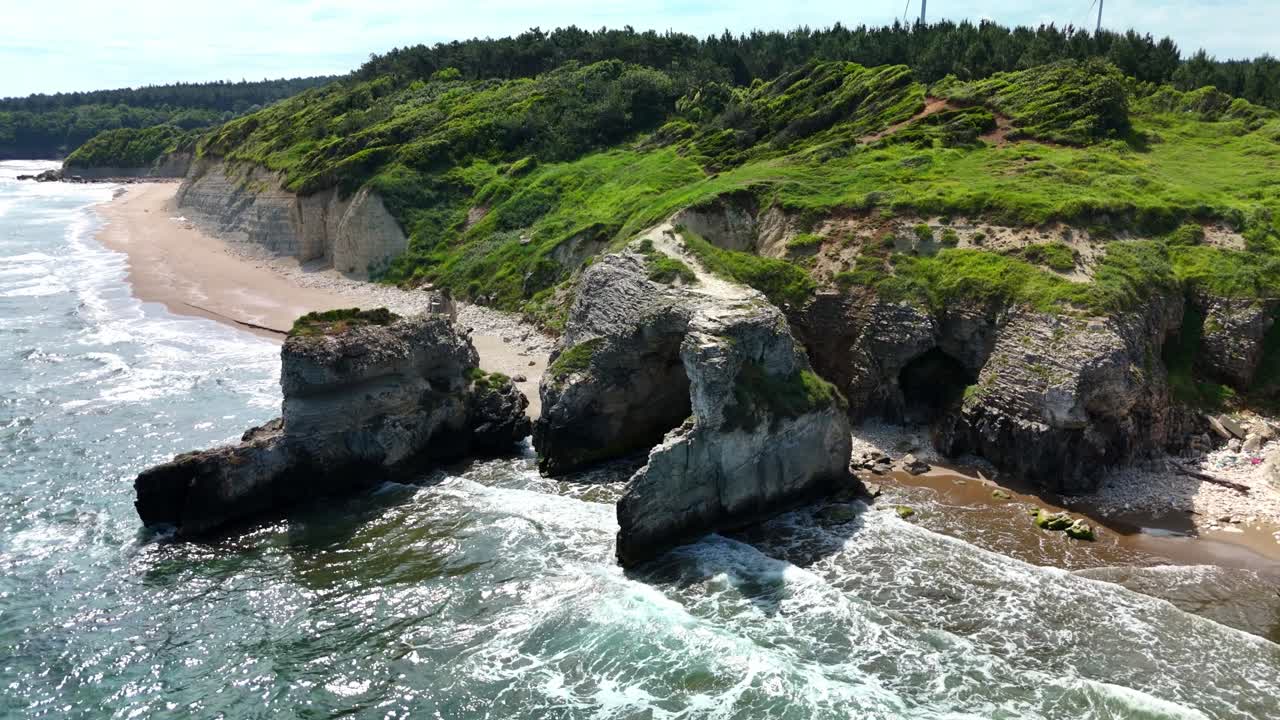 Wind turbines on a lush coastal hill with rocky shoreline waves