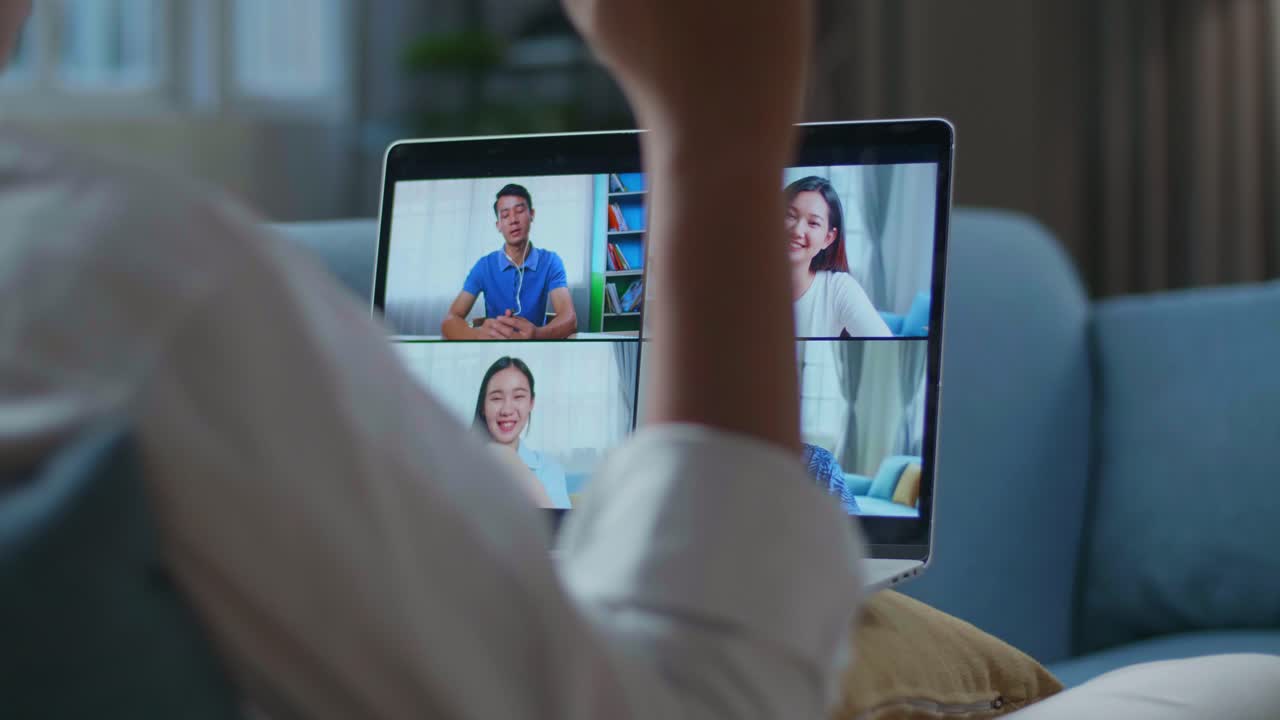 un hombre se saluda con sus colegas en una llamada de videoconferencia desde una computadora portátil mientras está tendido en el sofá en la sala de estar