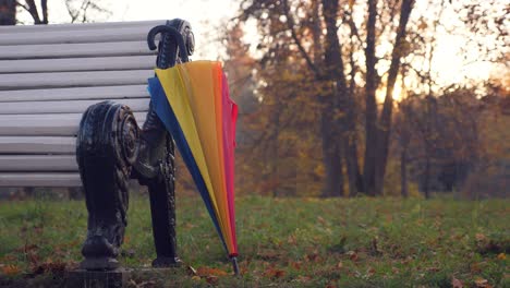 regenbogen-schirm auf einer parkbank im herbst