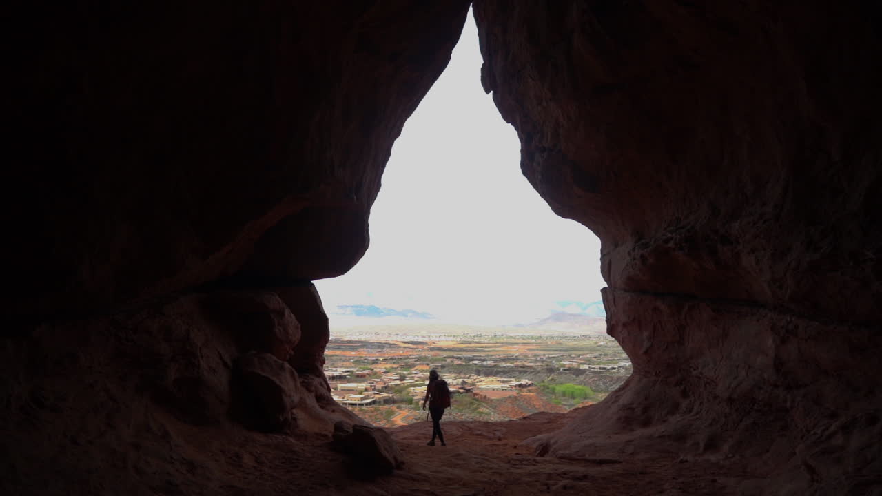 silueta de una excursionista caminando frente a la entrada de la cueva, en cámara lenta