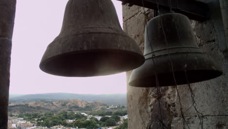 Church-bells-mounted-in-high-tower-in-the-public-square-of-a-small-mexican-town,-that-can-be-heard-by-the-surrounding-community