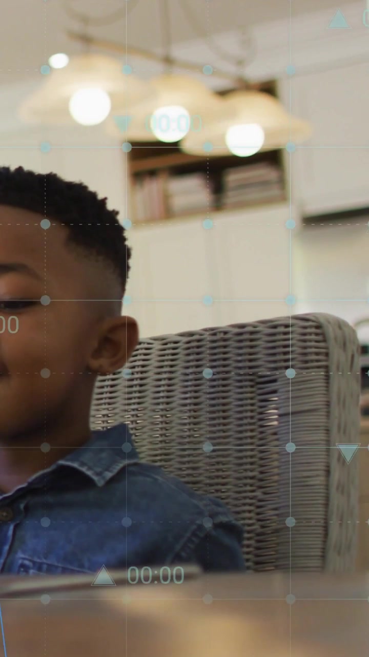 Boy glancing at tablet and speaking in home dining area, HUD grid animating charts for education