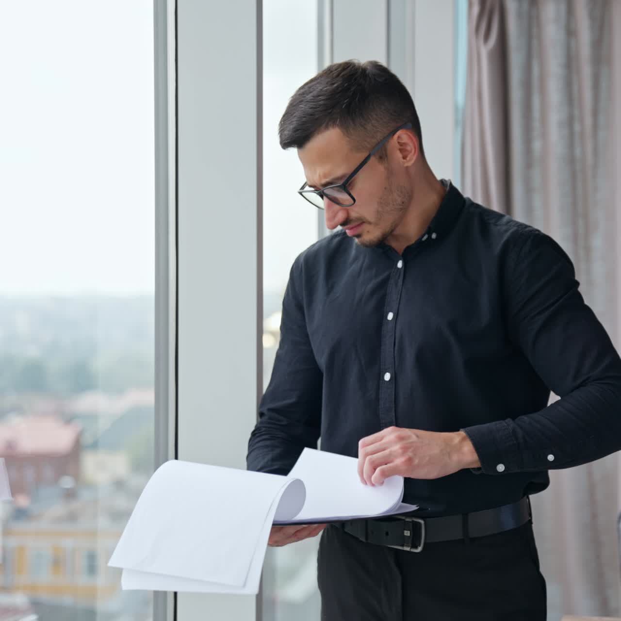 Worried man turning pages of report. Man in black clothes looks through the papers with charts with concerned expression on his face