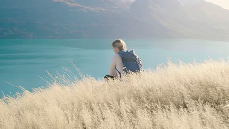 Niña-Sentada-En-La-Hierba-Dorada-En-Las-Montañas-De-Nueva-Zelanda-Con-Vistas-Al-Lago-Azul