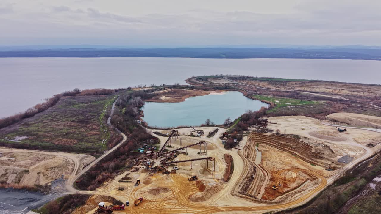 View of sand quarry by lake and hills with cloudy sky in background