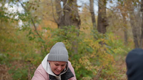 close-up of joyful relatives playing outdoors with dry autumn leaves, child throws leaves at her, she bends down to gather more and playfully pours them on him