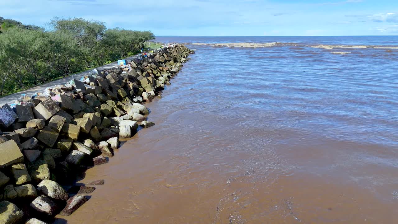 Aerial drone video gliding above geometric rock breakwater at river mouth, Nambucca, Australia