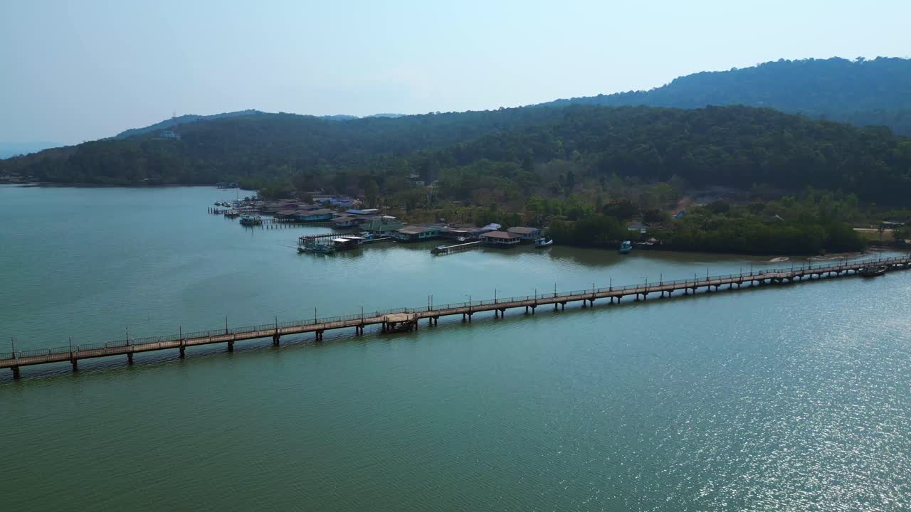 Coastal village with houses on stilts, boats and a long pier in a tropical bay. Dramatic aerial view fly push forward drone