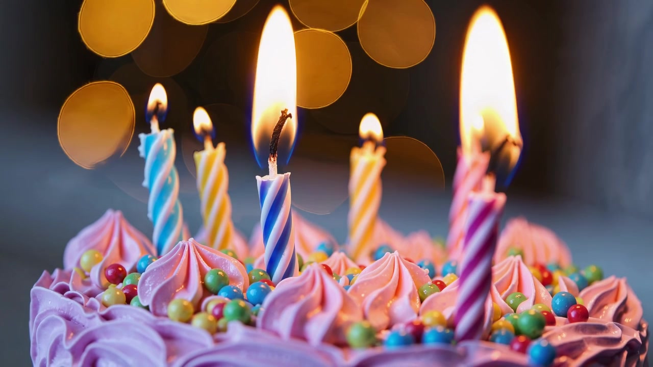 Primo piano di candeline di compleanno accese su una torta colorata con sfondo bokeh