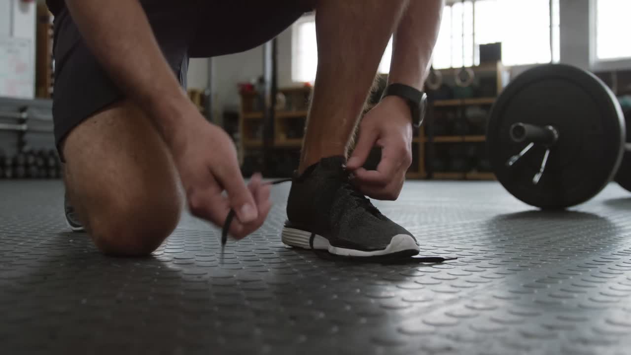 Vista frontale della parte inferiore di un uomo caucasico atletico che si allaccia le scarpe.