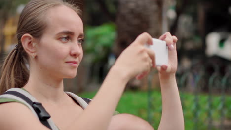 Carrying her infant in a kangaroo backpack, a young woman takes snapshots on a mobile phone during her travels. She walks and periodically gazes at the phone screen