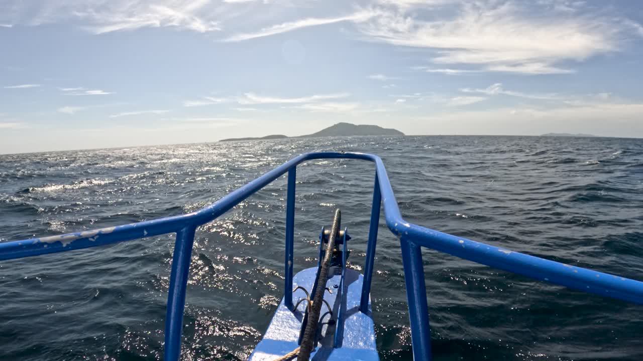 Blue boat moves toward distant island on sunny day, gentle waves, wide angle, natural lighting