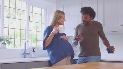 pareja madura con esposa embarazada en la cocina hablando y bebiendo café juntos