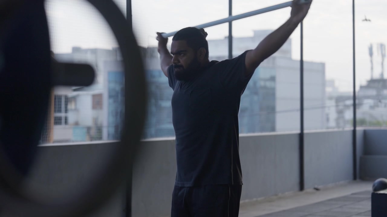 Bearded male athlete performing an upper-body mobility exercise with a dowel rod during a fitness training session in a modern indoor gym.