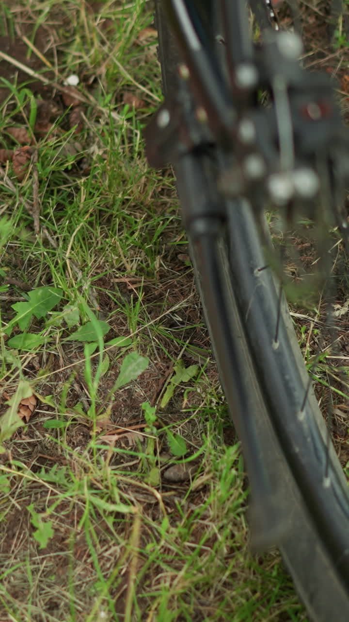 primer plano del pie de una persona con zapatillas rosadas quitando el soporte de la bicicleta, colocado en un terreno cubierto de hierba con un fondo borroso de la rueda de la bicicleta y un parque verde exuberante