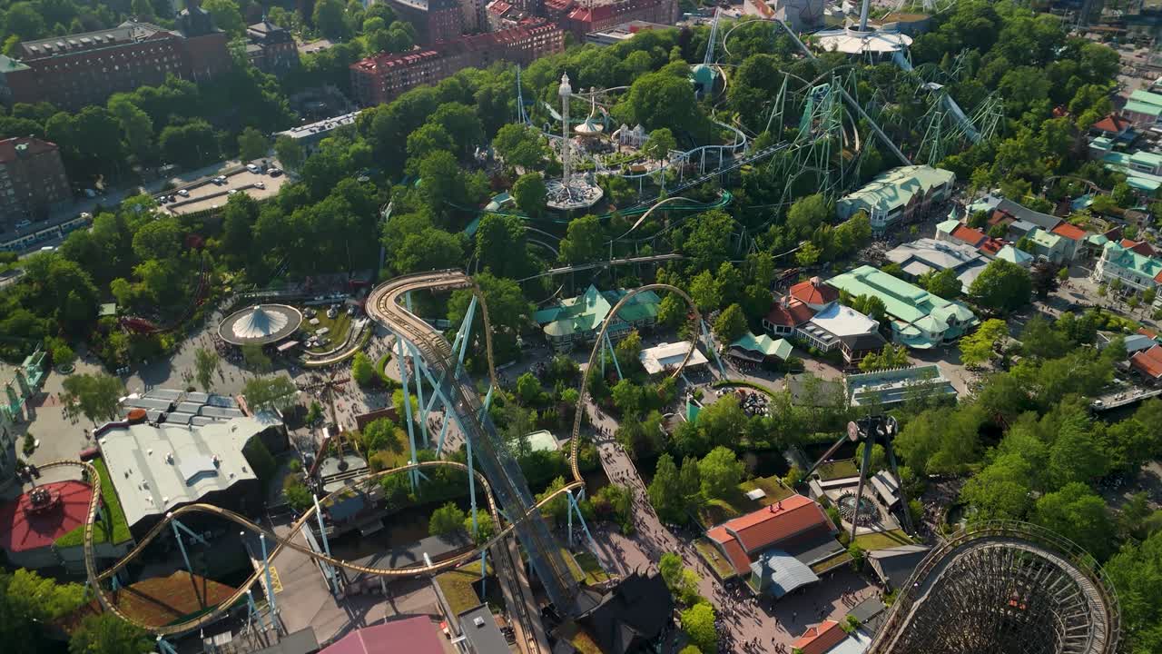 Dramatisk luftbåren parallakse som trekker seg tilbake fra tre-berg-og-dal-bane-sporene på Liseberg for å avsløre hele fornøyelsesparken og en vidstrakt bysilhuett av Gøteborg.