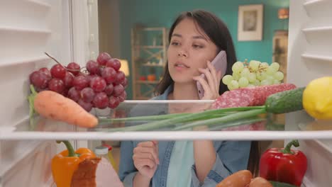 woman checking fridge inventory while talking on the phone