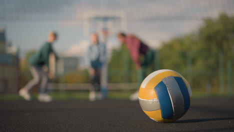 close-up of volleyball on ground with blurred background of people exercising, stretching, and working out outdoors, the shot highlights vibrant athletic activity and dynamic fitness