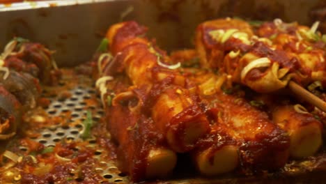 fish cake skewers with spicy red sauce and chopped green onions. korean street food. closeup sliding shot