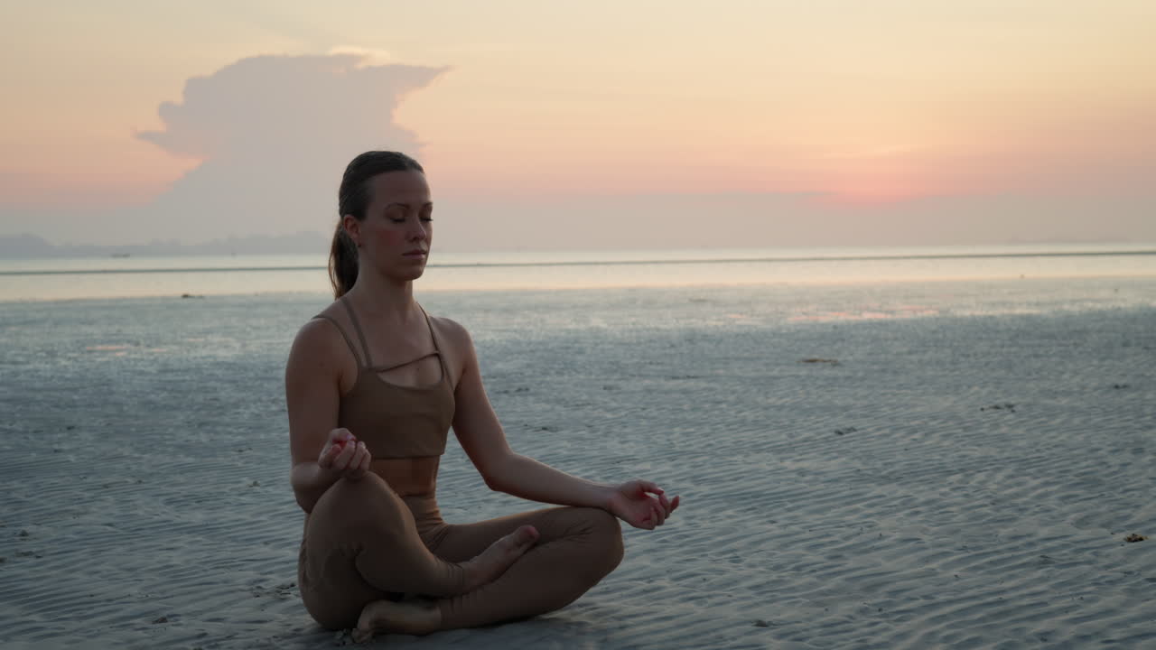Joven mujer practicando meditación de yoga en la playa al atardecer