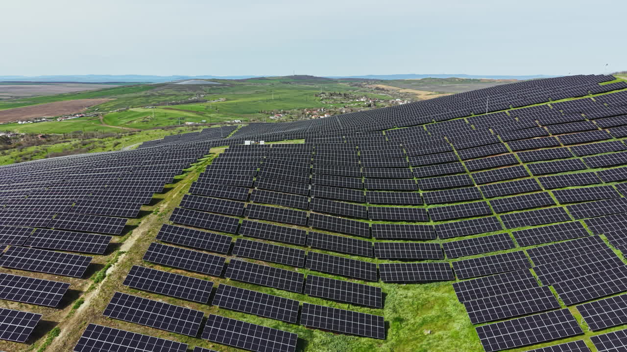 Solpaneler dækker bakker i en stor solcellepark beliggende i et landområde under en klar himmel i dagtimerne.
