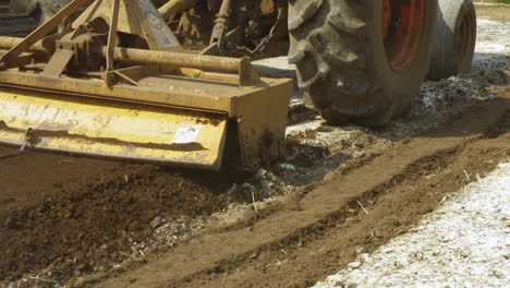 Close-up-of-tractor-implement-know-as-rear-blade,-preparing-hard-old-field-with-a-rotary-tiller,-slow-motion