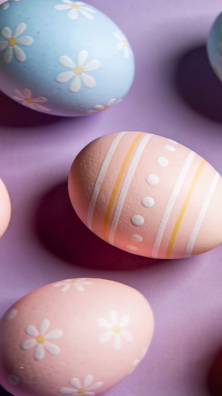 Panning camera over hand-painted pastel eggs on purple surface, revealing daisy and stripe details