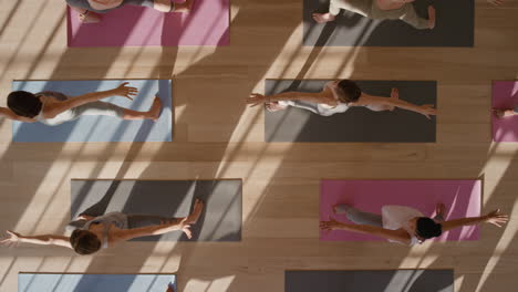 Vista-Superior-Clase-De-Yoga-Mujeres-Sanas-Practicando-Pose-Guerrera-Disfrutando-De-Un-Estilo-De-Vida-Fitness-Haciendo-Ejercicio-En-El-Estudio-Al-Amanecer