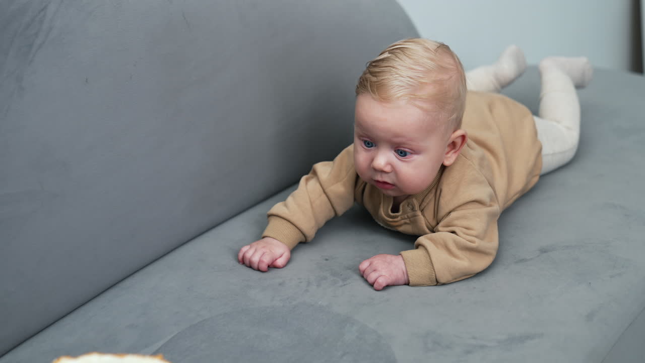 Lovely blond baby boy lies on the belly in front of a cake. Blue-eyed kid looks at the dessert attentively.