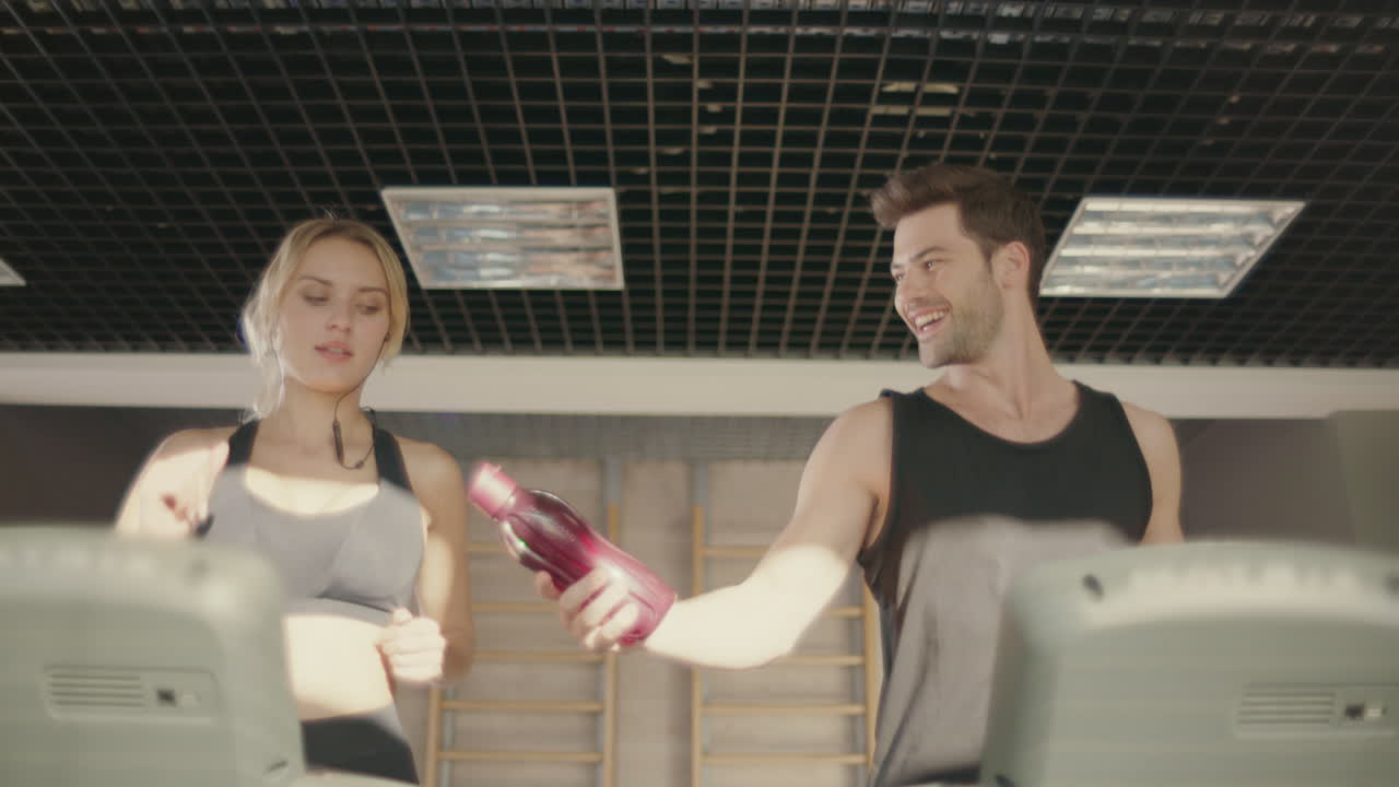 hombre guapo coqueteando con una mujer en una máquina de caminadora en un club de fitness.