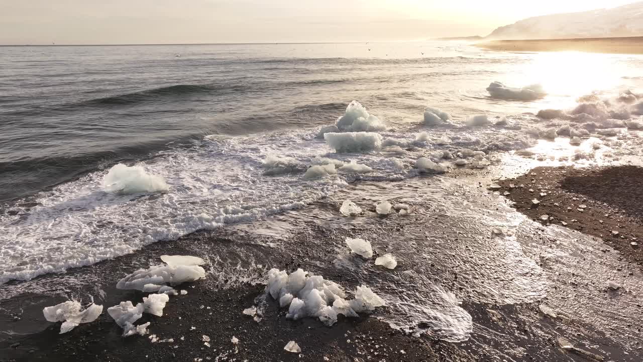 Drone flight over crashing waves and ice chunks scattered along the volcanic shore of Diamond Beach, Jökulsárlón, Iceland.