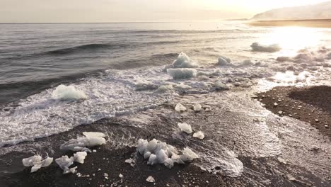 drone flight over crashing waves and ice chunks scattered along the volcanic shore of diamond beach, jökulsárlón, iceland.